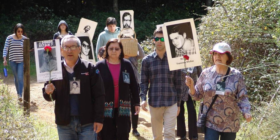 Verschiedene Personen demonstrieren in einer Grünanlage und halten dabei Schilder von Todesopfern der Colonia Dignidad hoch