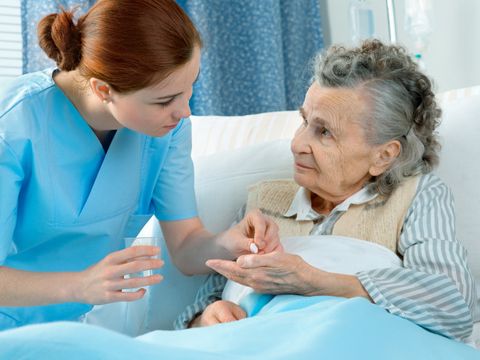 Krankenschwester kümmert sich um eine ältere Frau im Bett liegend