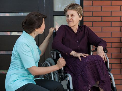 Pflegerin kniet neben einer Frau in einem Rollstuhl