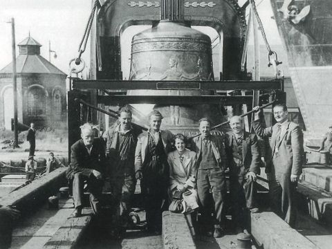 Bildvergrößerung: Sechs Männer und eine Frau vor einer großen Glocke lächeln in die Kamera