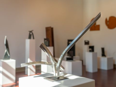 Im Vordergrud eine silberfarbene Kunstskulptur. Einzelne stränge der Instalation sind in unterschiedliche Richtungen verbogen. 