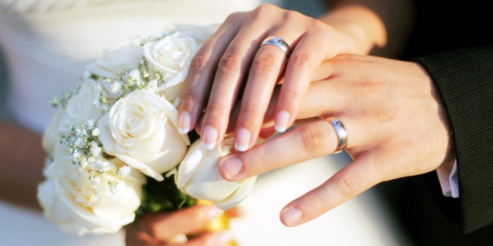 Hände eines Hochzeitpaares mit Eheringen vor dem Brautstrauss