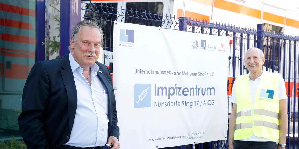 Zwei Männer stehen vor einem Schild mit der Aufschrift "Impfzentrum".