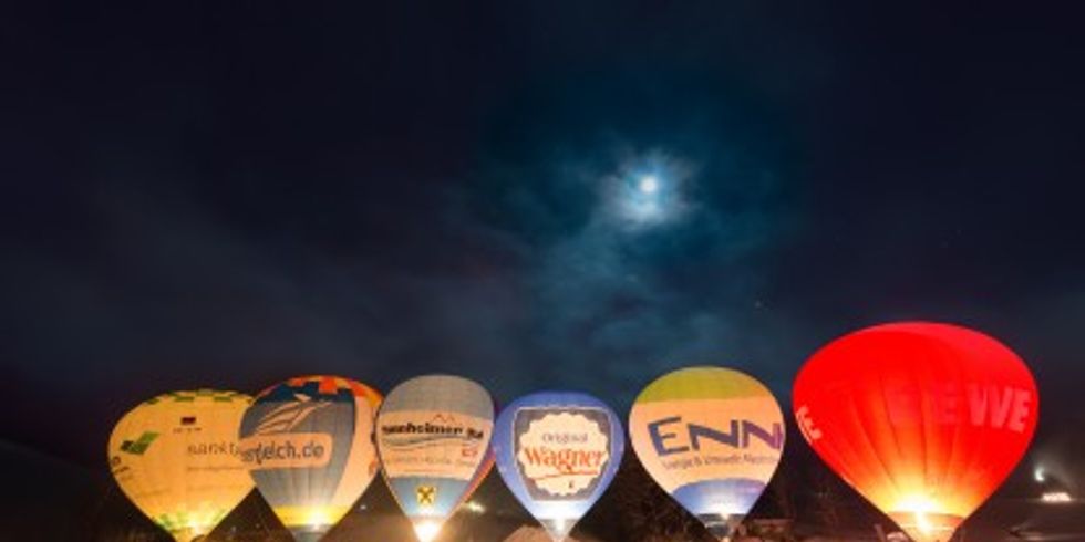 sechs Heißluftballons am Boden, welche gerade zur Abfahrt bereit gemacht werden