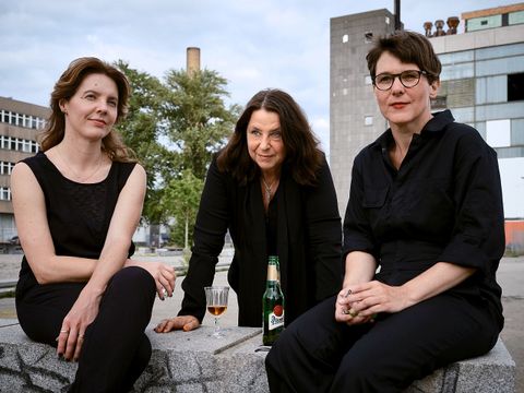 Die drei Autorinnen Annett Gröschner, Peggy Mädler und Wenke Seemann sitzen mit Getränken auf einer Mauer