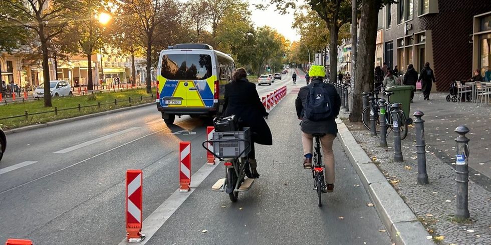 Zwei Personen fahren auf einer geschützten Radverkehrsanlage Fahrrad.