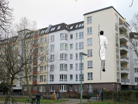 Bildvergrößerung: Auf der Fassade eines Hauses ist das Bild von einem Arzt, der in einem Riss in der Hauswand verschwindet.