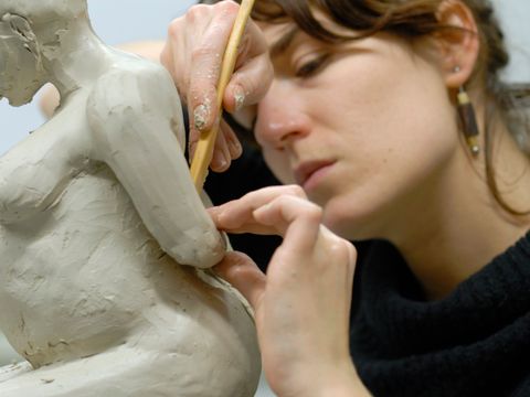 Teilnehmerin im Bildhauerkurs modelliert eine menschliche Figur