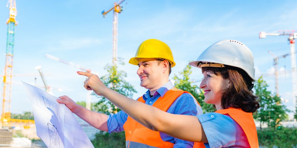 Zwei Mitarbeiter mit Bauhelmen vor einer Baustelle