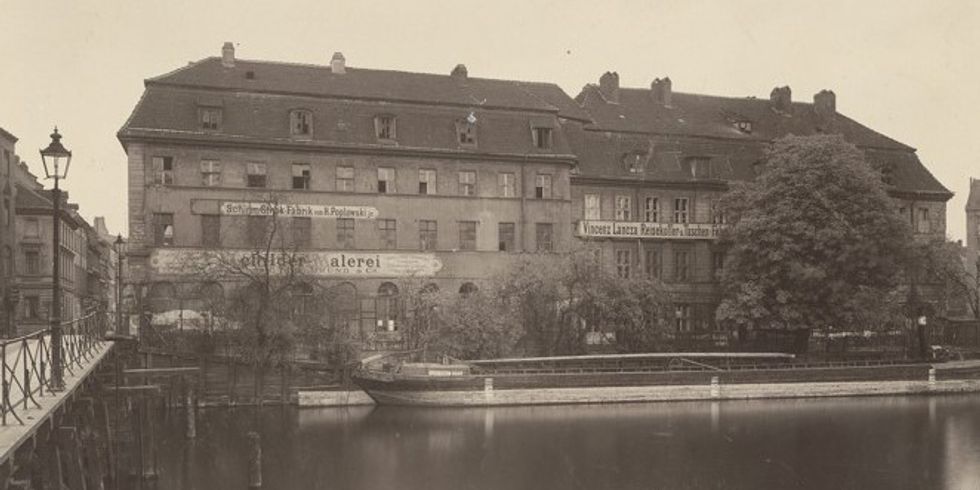 Inselbrücke und Inselgebäude an der Fischerbrücke 17 kurz vor ihrem Abriss, davor die Hafenkastanie. Links die hölzerne Inselbrücke, in Verlängerung der Brücke das Eckhaus An der Fischerbrücke 15 (ehem. Wegely‘sches Haus), mittig und rechts im Bild die ehemaligen Fabrikgebäude der Wegely’schen Wollzeugfabrik.Langhans Carl Ferdinand (1782-1869): Inselspeicher, Berlin-Mitte.