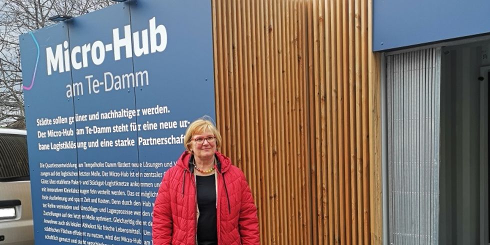 Frau steht vor einem eckigen Bauwerk mit Eingang mit der Aufschrift Micro-Hub am Te-Damm