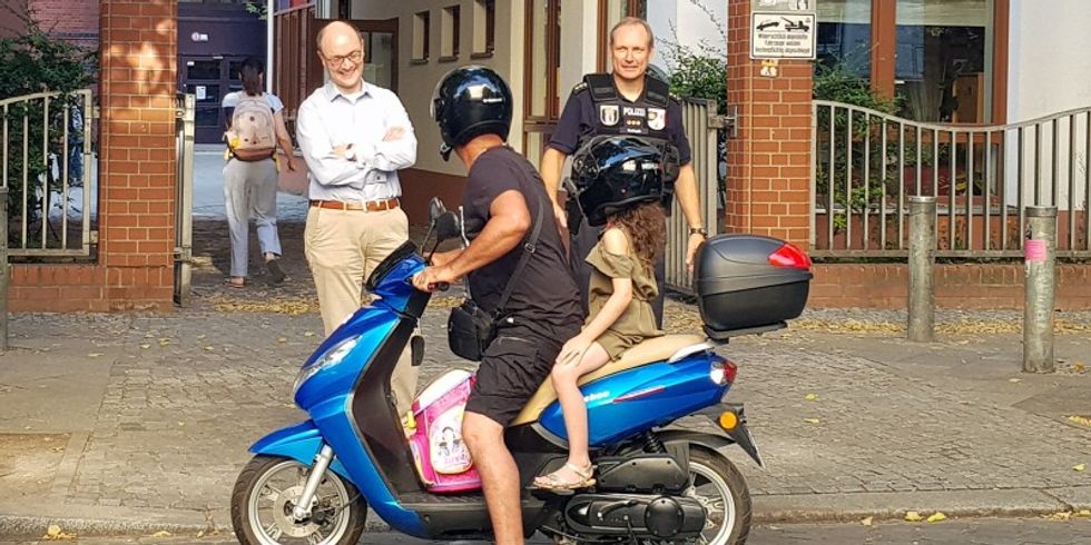 Arne Herz, Stadtrat für Ordnungsangelegenheiten (l.) und Andreas Tschisch, Leiter des Polizeiabschnitts 25, bitten einen Roller-fahrenden Vater, sein Fahrzeug nicht in der Einfahrt der Joan-Miró-Schule abzustellen.