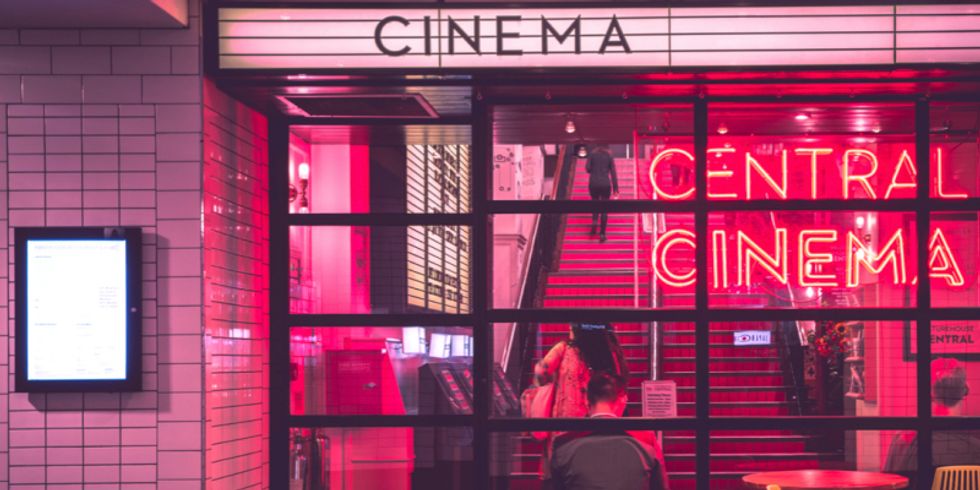 Blick durch Fenster in rot beleuchteten Raum mit vier Personen darin und darüber auf einem Schild das Wort "Cinema"