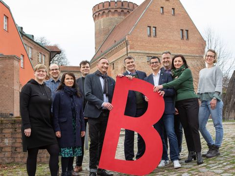 Die Teilnehmer und Teilnehmerinnen der Pressekonferenz vor dem Juliusturm mit den großen roten "B"