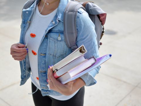 Eine junge Frau in Jeansjacke trägt einen Stapel Bücher auf dem Arm