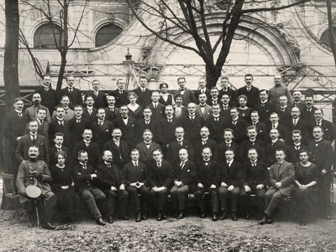 Bildvergrößerung: Schwarz-weiß-Fotografie von einer Gruppe Menschen, dieauf einer Grünfläche posiert auf Bänken sitzen und stehen.
