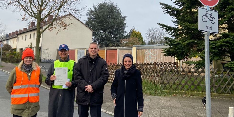 Vier Personen stehen auf einer Straße neben einem Schild, dass den Weg für Radfahrende freigibt.