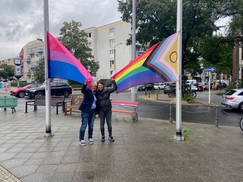 Diversity- und Queerbeauftragte, Sabine Pöhl, und Bezirksstadträtin Filiz Keküllüoğlu (Bündnis 90 / Die Grünen) halten die beiden Fahnen.