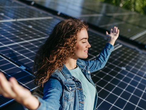 Frau lächelnd in Yogaposition auf dem Dach, Solaranlage im Hintergrund