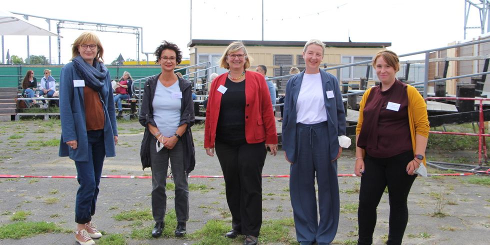 Fünf Frauen stehen nebeneinander auf einem Platz und lächeln in die Kamera.