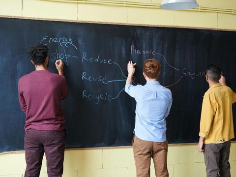 Drei Männer unterschiedlichen Alters stehen an einer schwarzen Tafel und schreiben