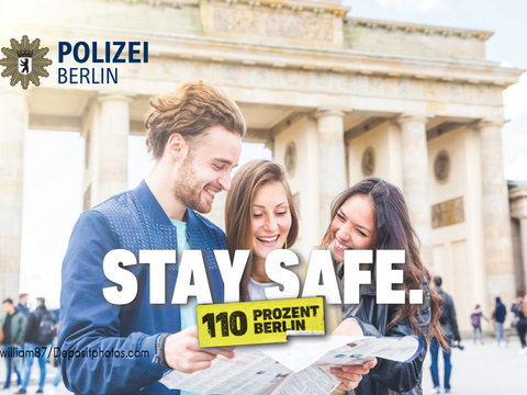 Personen mit einer Karte vor dem Brandenburger Tor darüber Schriftzug Stay Safe 110 Prozent Berlin