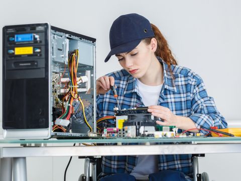 Junge Frau im Rollstuhl repariert Computer