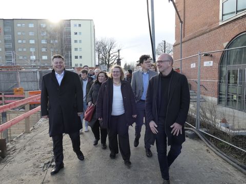 Bildvergrößerung: Eine Gruppe Menschen läft auf einer Baustelle neben einem Gebäude entlang.