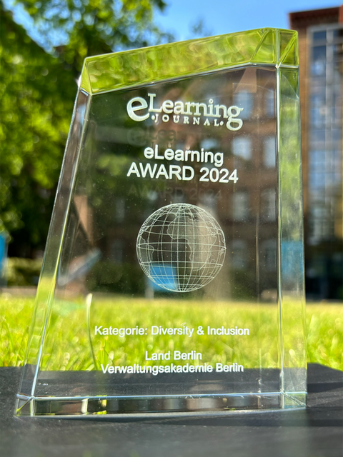 Der eLearning Award ist aus Glas und steht im Sonnenlicht vor der Verwaltungsakademie im Gras.