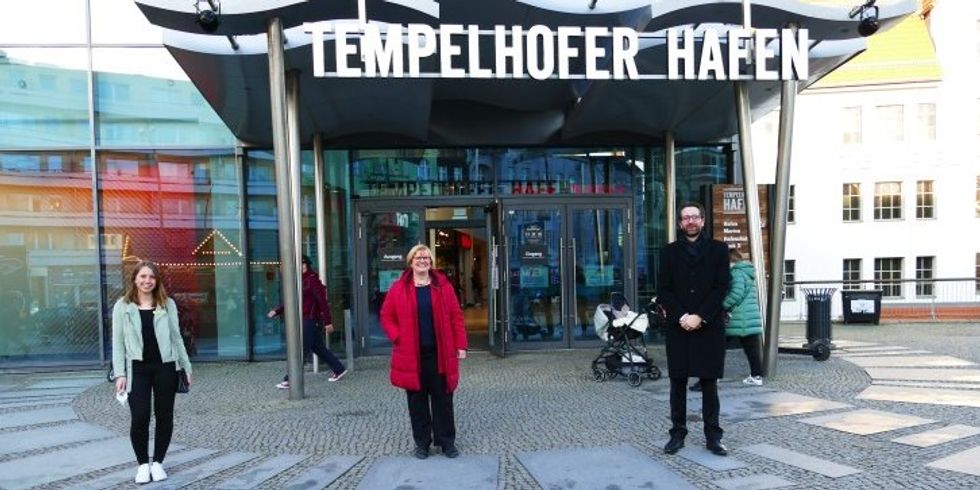 Drei Personen stehen vor einem Gebäude mit der Aufschrift Tempelhofer Hafen