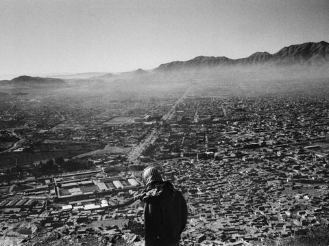 Bildvergrößerung: Eine schwarz-weiß Fotografie. Ein Mann mit Kopftuch steht auf einem Berg und schaut hinab in eine Stadt im Tal. Im Hintergrund sieht man Nebel und Gebirge.