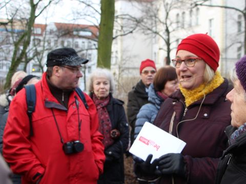 Bildvergrößerung: eine Frau spricht vor winterlich bekleideten Menschen auf der Straße. 