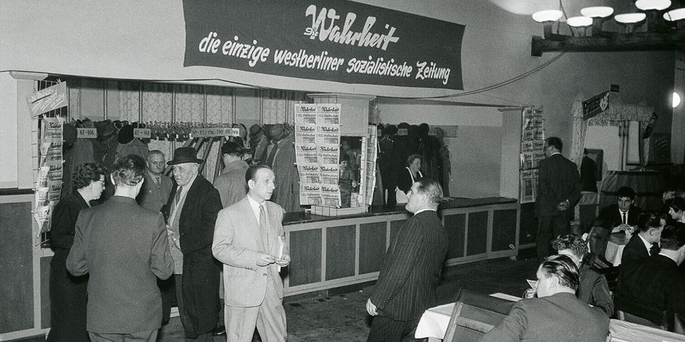 Eine Schwarz-Weiß-Fotografie eines Festes in einer Halle. Auf einem Banner steht der Schriftzug "Die Wahrheit, die einzige westberliner sozialistische Zeitung".