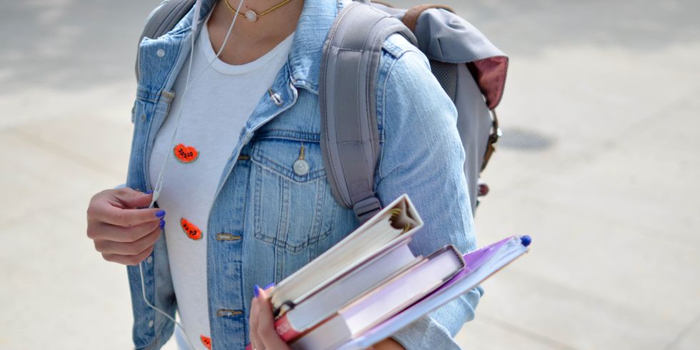 Eine junge Frau in Jeansjacke trägt einen Stapel Bücher auf dem Arm