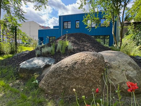 Vulkanskulptur aus Lavagestein im Gartenbereich und im Hintergrund ein blaues Haus