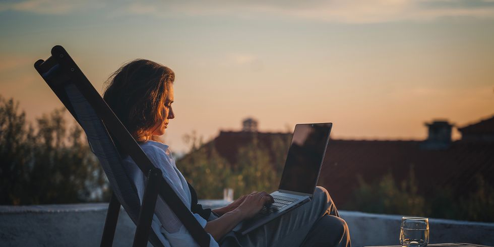 Frau auf Dach in Liegestuhl mit Laptop, Sonnenuntergang