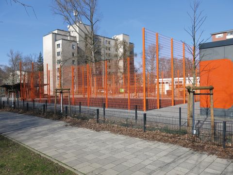 Ballfangzaun in Orange, Wohnhochhaus, neu gepflanzte Bäume im Winter