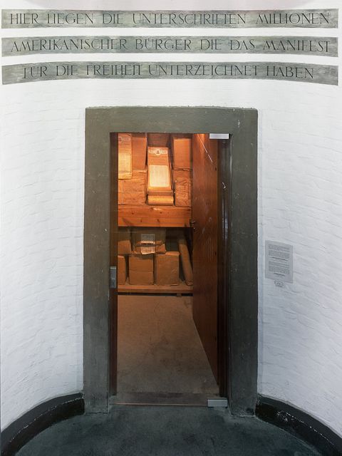 Open door with an inscription above the entrance; the interior is lit and shows packages wrapped in brown paper. 