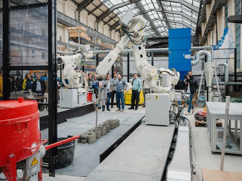 Menschen in einer Fertigungshalle neben einem großen Roboterarm