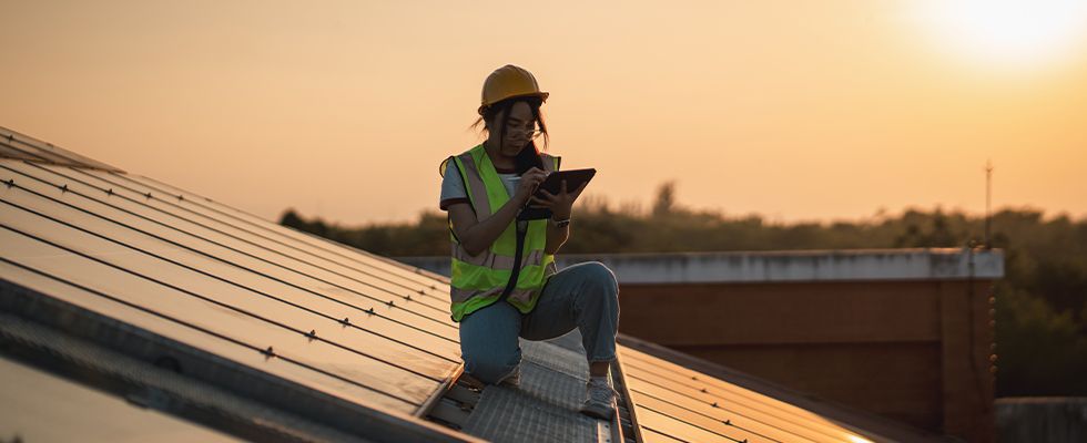 Frau auf den Dach zwischen Solarpanels mit Tablet in der Hand