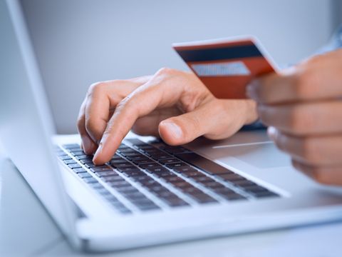 Eine Person hält mit der linken Hand eine Chipkarte vor sich und tippt mit der rechten Hand auf der Tastatur eines Laptops