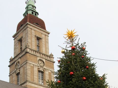 eine weihnachtlich geschmückte Tanne vor einem großen Gebäude mit Turm