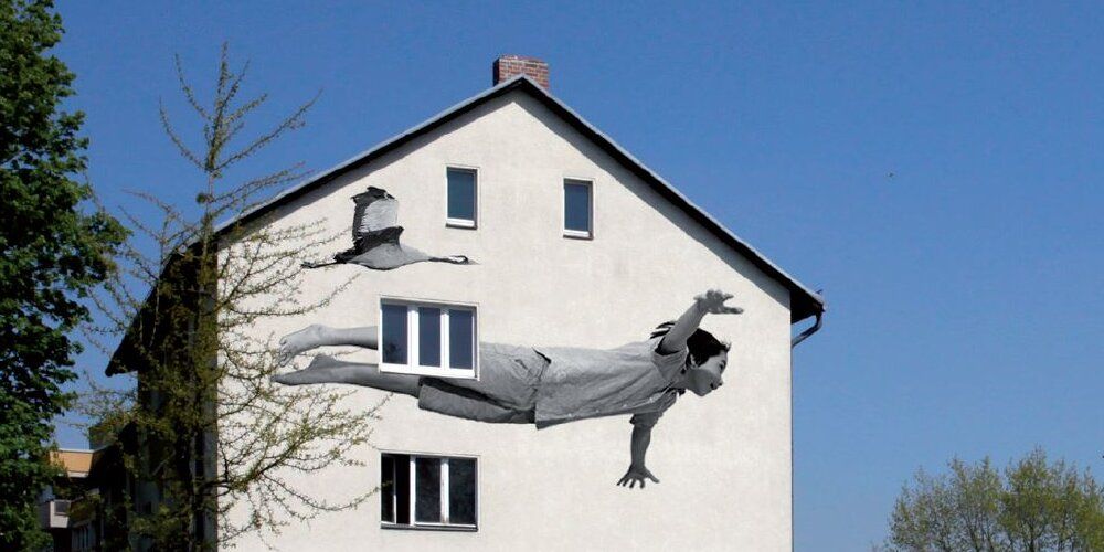 Auf der Fassade von einem Haus ist ein schwarz-weiß Bild von einem scheinbar fliegendem Kind.