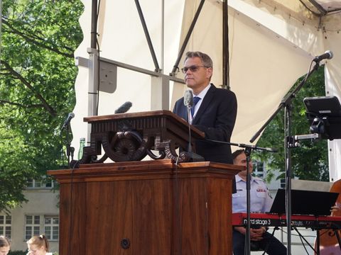 Bildvergrößerung: Ein Mann steht auf einer Bühne hinter einem hölzernen Rednerpult mit Mikrofonen.