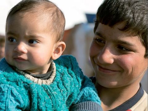 Junger lächelnder syrischer Flüchtling mit Baby auf dem Arm
