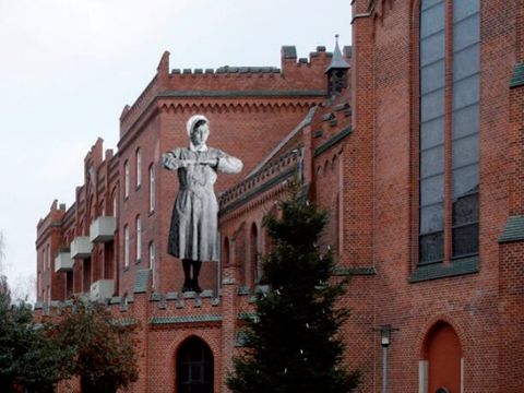 Bildvergrößerung: Auf einem Backsteingebäude ist ein schwarz-weiß Bild von einer Krankenschwester abgebildet.