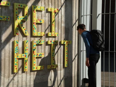 Ein Besucher der Gedenkstätte Hohenschönhausen steht vor einer Betonwand mit den gelben Buchstaben "Freiheit".