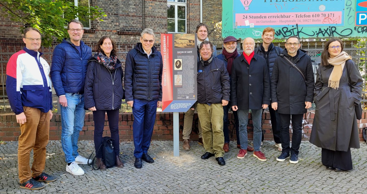 viele Menschen stehen neben einer Tafel vor einem Gebäude