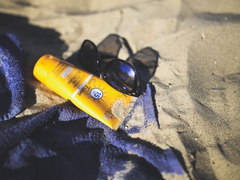 Sonnencreme, Sonnenbrille und Handtuch im Sand