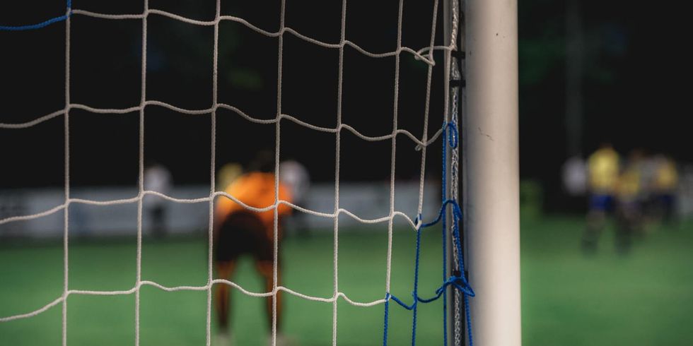 Perspektive hinter dem Tor mit Torwart und weiteren Feldspielern verschwommen im Hintergrund.